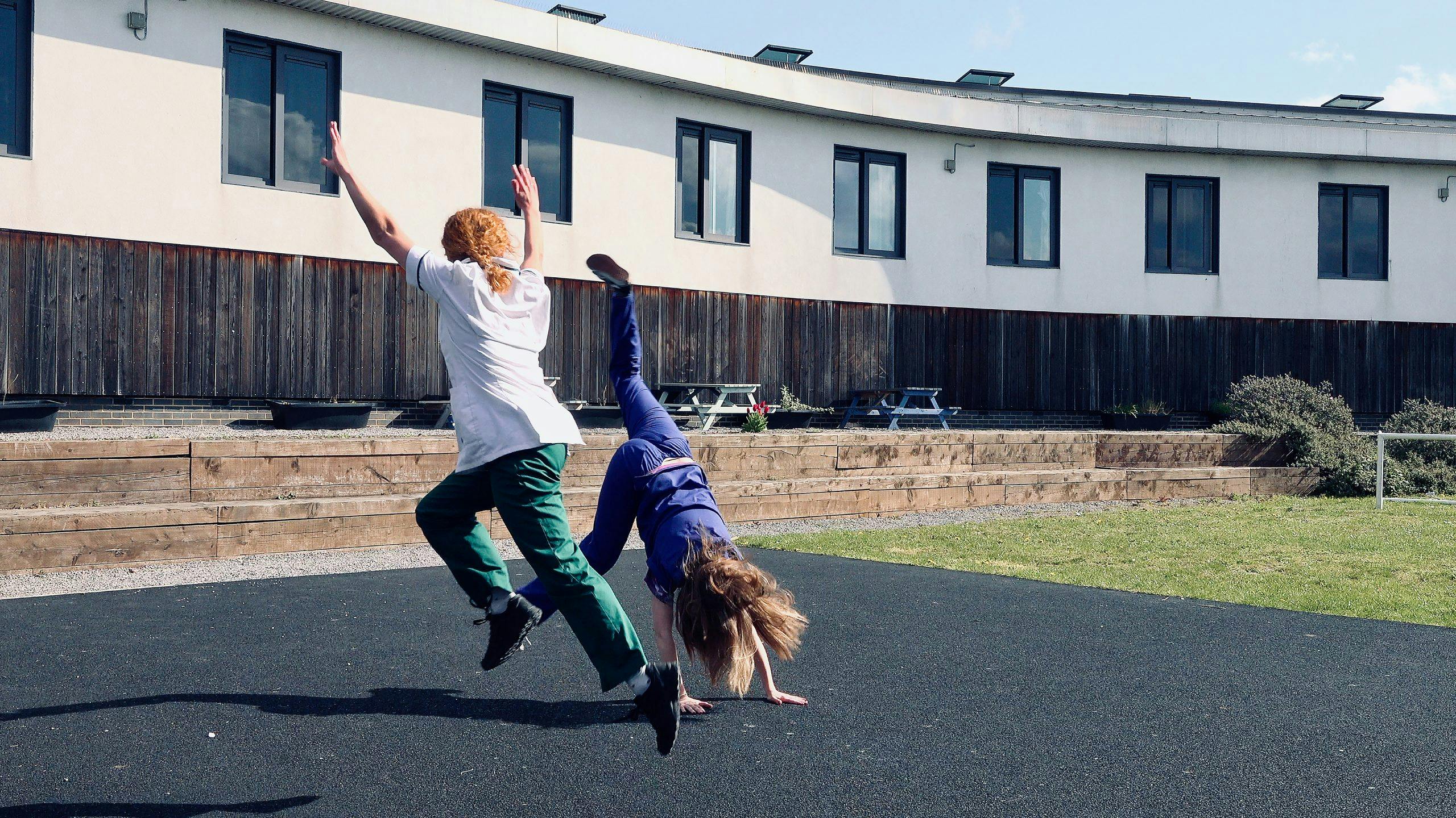 Two nurses dressed in their uniforms doing cartwheels. 