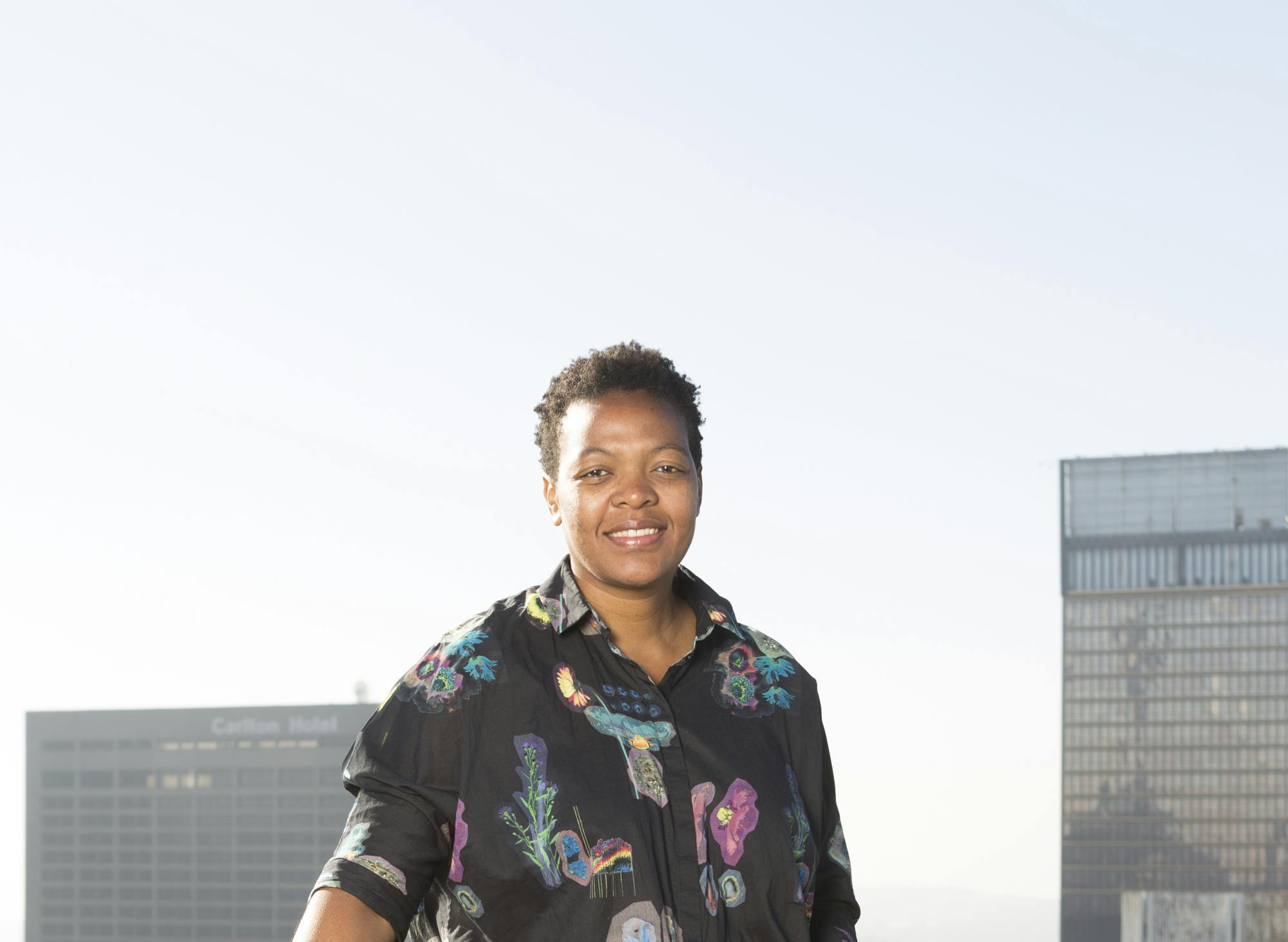 A woman appears contend and smiling wearing a colourful shirt. She appears against clear blue sky. 