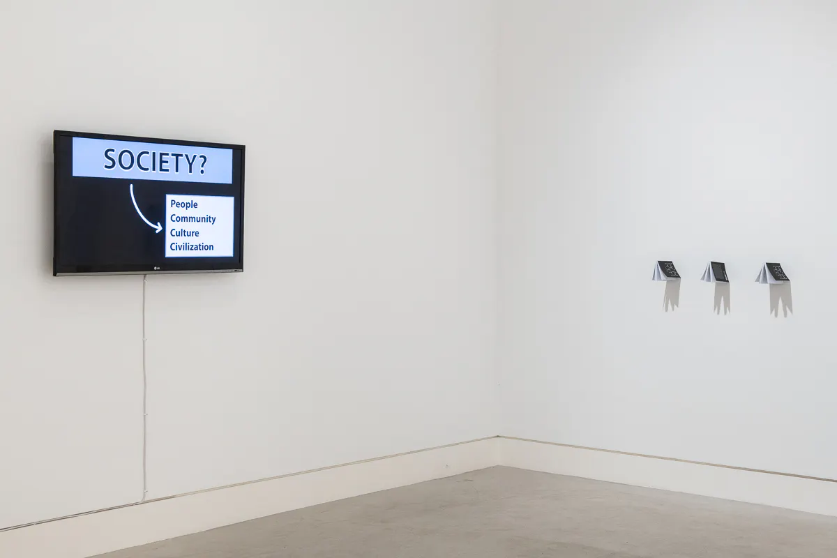 A flat screen TV on the left of the image has a screen that says Society ? To the right of the image is a series of publications on the wall, their shadows form the shape of birds.