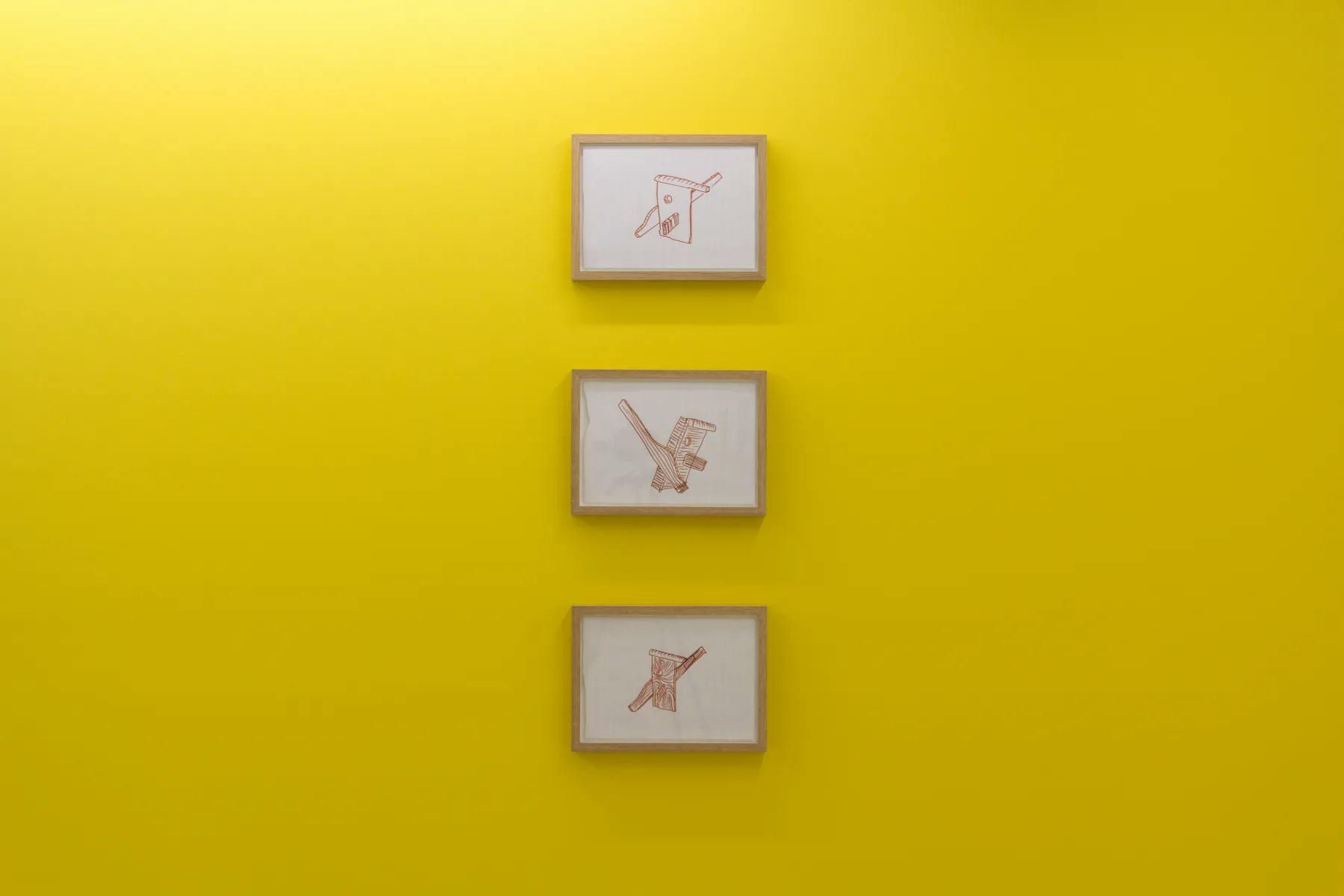 A mustard coloured wall with framed drawings of timber and furniture forming funning cartoon like faces.