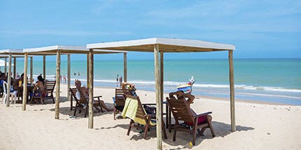 Imagem da praia em Porto Seguro, Bahia, em dia ensolarado. A foto mostra turistas na praia, sentados em cadeiras com guarda-sóis, admirando o mar cristalino.