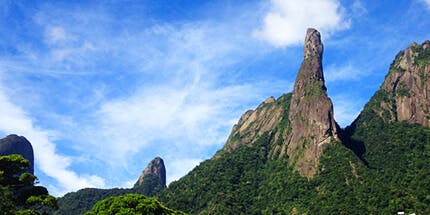 Imagem da Travessia Petrópolis em Teresópolis, no Rio de Janeiro. A foto mostra o pico em dia ensolarado, com foco em suas montanhas pontiagudas cercadas pela vegetação local.