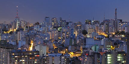 Imagem da cidade de São Paulo ao anoitecer com a paisagem de prédios e luzes.