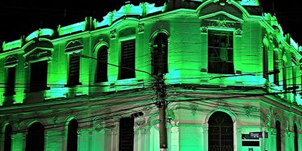 Imagem do Centro Cultural de Pouso Alegre, em Minas Gerais à noite. O prédio branco está iluminado com uma luz forte e verde.