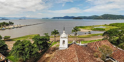 Imagem da costa de Paraty, no Rio de Janeiro, em dia ensolarado. A foto mostra o mar com montanhas ao fundo.