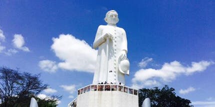 Imagem da Estátua do Padre Cícero na colina do Horto em Juazeiro do Norte, no Ceará. A foto mostra a estátua branca contra o céu ensolarado e azul.
