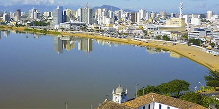 Imagem panorâmica da cidade de Campos dos Goytacazes, no Rio de Janeiro, em dia ensolarado. A foto mostra a paisagem de prédios com montanhas ao fundo.