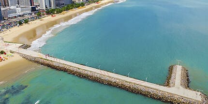 Imagem panorâmica da praia de Fortaleza no Ceará em um dia ensolarado, com o mar claro e azulado.