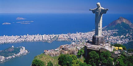 Imagem do Cristo Redentor em dia ensolarada com vista da costa do Rio de Janeiro.
