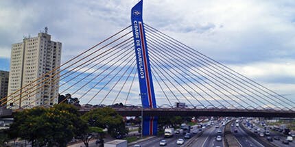 Imagem da entrada da cidade de Guarulhos, em São Paulo, em dia ensolarado. A foto mostra a Ponte de Guarulhos, que marca a entrada da cidade.