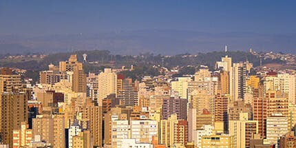 Imagem panorâmica da cidade de Campinas, em São Paulo, ao amanhecer. A foto mostra a paisagem de prédios com montanhas ao fundo.