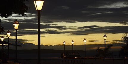 Imagem de São Luís do Maranhão ao entardecer. A imagem mostra uma ponte, com luzes em postes acesas enquanto o sol se põe. 