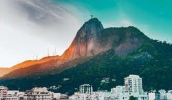 Imagem da cidade do Rio de Janeiro, com prédios em primeiro plano. A estátua com o Cristo Redentor está ao fundo, cercada pela vegetação local.