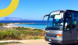 Imagem de um ônibus de viagem estacionado em frente à praia em dia ensolarado com céu azul.