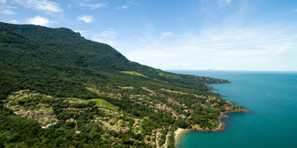 Imagem da costa de Ilhabela em dia ensolarado, mostrando o mar azul e vegetação da região.