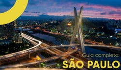 Imagem da Ponte Estaiada da cidade de São Paulo ao anoitecer, com as luzes da cidade acesas e céu azulado. Na imagem há a imagem "Guia completo: São Paulo".