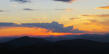 Imagem do pôr-do-sol com vista do Pico Agudo em Santo Antônio do Pinhal em São Paulo. A foto mostra montanhas contra a luz do sol com o céu alaranjado.