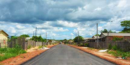 Imagem da cidade de Rorainopolis, em Roraima. A foto mostra uma das ruas da cidade em um dia ensolarado, com casas e árvores de ambos os lados da rua.