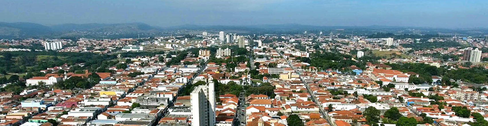 Foto aérea de Itu, no interior de São Paulo, com vista dos prédios, casas e árvores da cidade, com o céu azul e limpo no horizonte. 