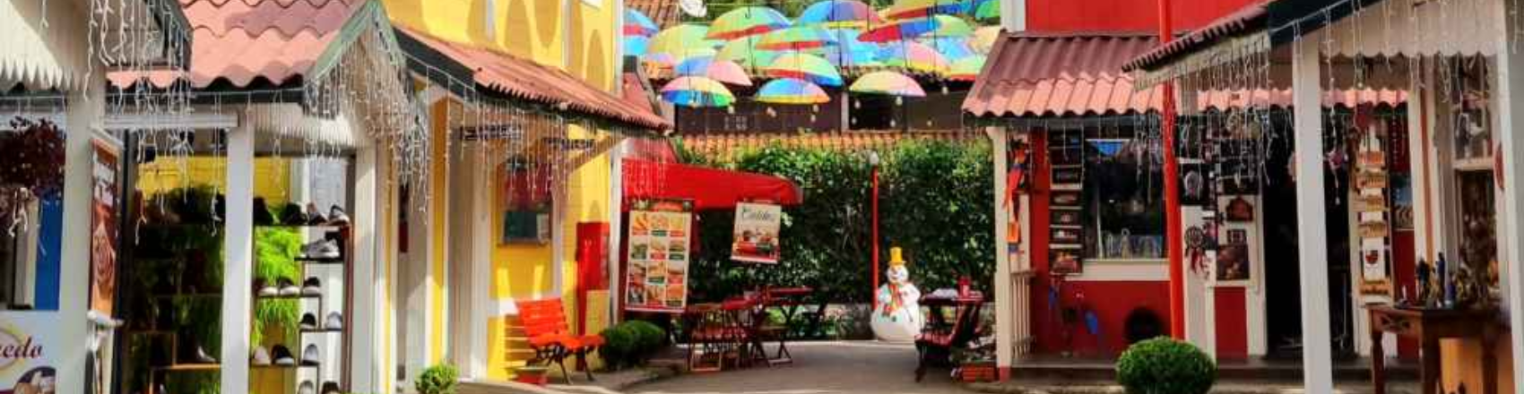 Registro de uma rua tradicional de Penedo, no Rio de Janeiro, com casas coloridas de vermelho e amarelo, e guarda-chuvas de decoração no alto. Há também pôsteres exibindo os produtos e serviços dos estabelecimentos.  