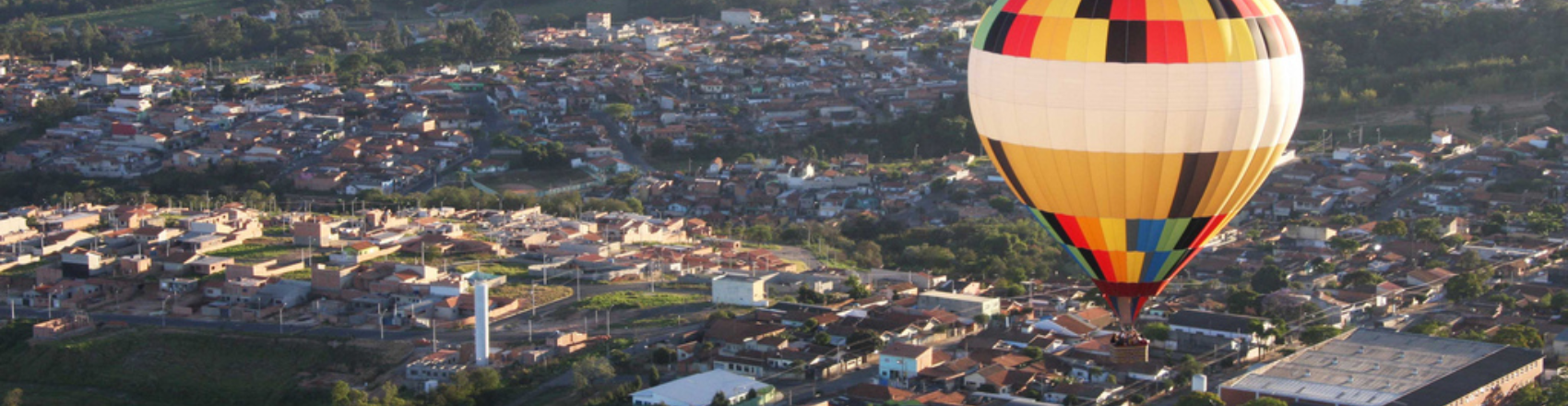 Vista aérea da cidade de Boituva, em São Paulo, com prédios e casas abaixo e um balão de ar colorido à direita. 