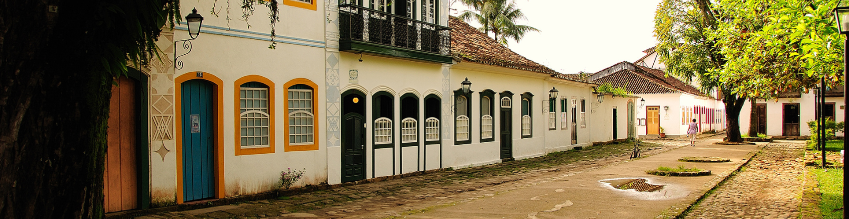 Centro de Paraty com destaque nas construções antigas característica da cidade: casas antigas com portas coloridas e a rua pavimentada com pedras irregulares.