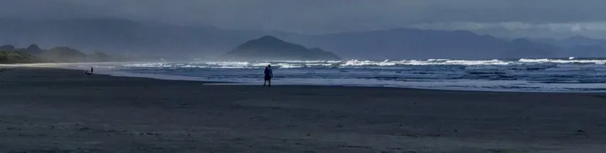 Bertioga no final de tarde com extensa faixa de areia com banhistas caminhando e mar agitado