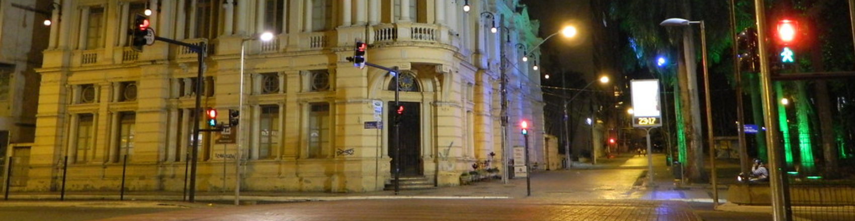 Prefeitura Municipal de Juiz de Fora a noite. A rua está iluminada com sinais de trânsito em vermelho. 