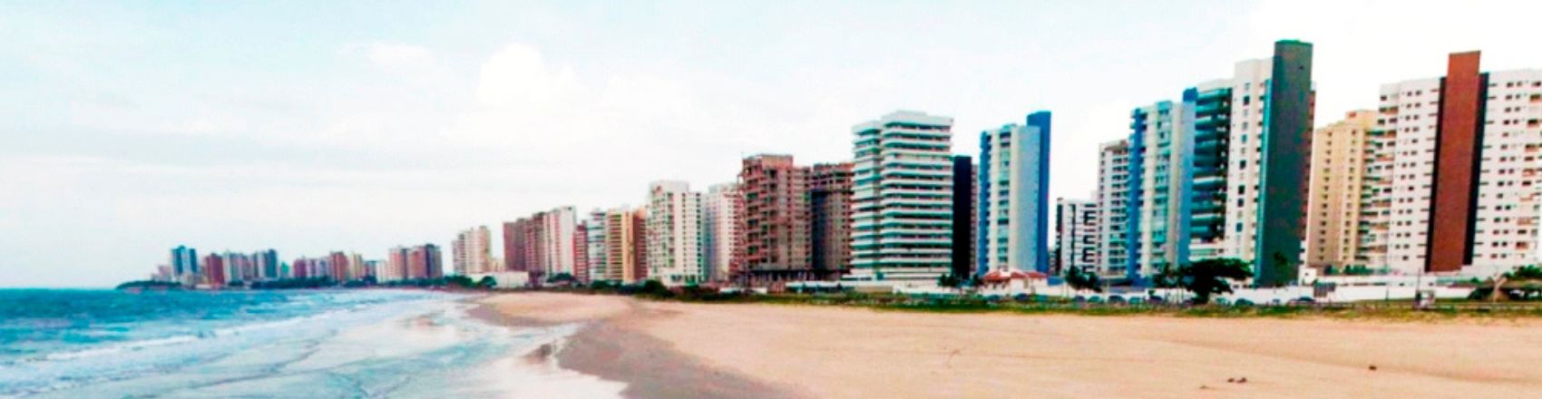 Praia em São Luís do Maranhão com prédios à beira-mar, uma extensa faixa de areia e o mar azul. 