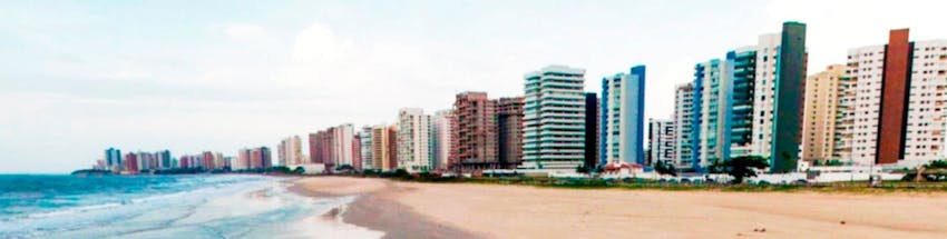 Praia em São Luís do Maranhão com prédios à beira-mar, uma extensa faixa de areia e o mar azul.