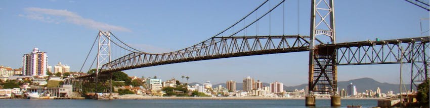 Ponte Hercílio Luz em Florianópolis, Santa Catarina. A foto mostra a ponte em primeiro plano e os prédios na linha do horizonte.