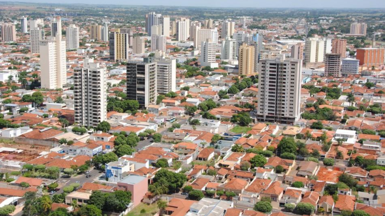 Vista de cima de prédios e casas de Araçatuba em dia de sol, com algumas árvores ao longo da cidade.