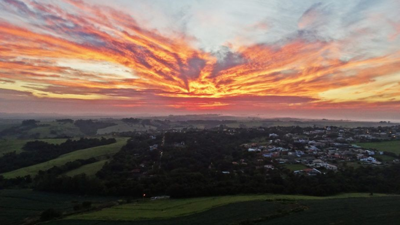 Pôr do sol em Boituva, em São Paulo, com construções ao fundo e área verde em primeiro plano.