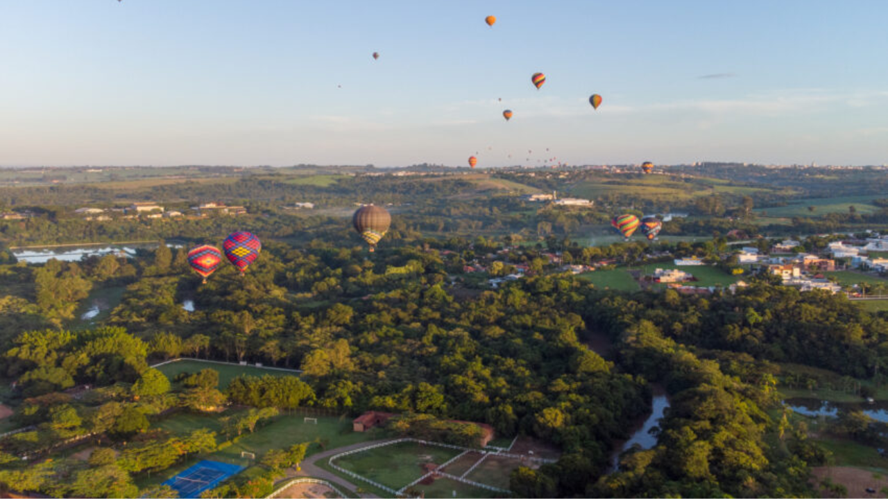 Céu de Boituva com diversos balões de ar coloridos voando e uma vasta área verde composta por árvores embaixo.