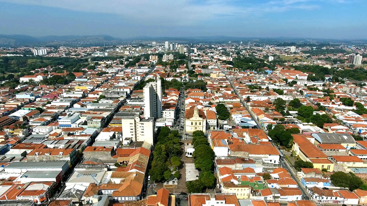 Vista de cima de Itu, com casas e prédios se misturando em meio às arvores. Ao fundo, vemos um céu limpo e azul claro.