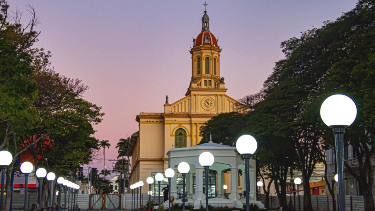 Itu ao entardecer, com a Catedral atrás e, na frente, os postes já ligados iluminando a calçada da igreja.