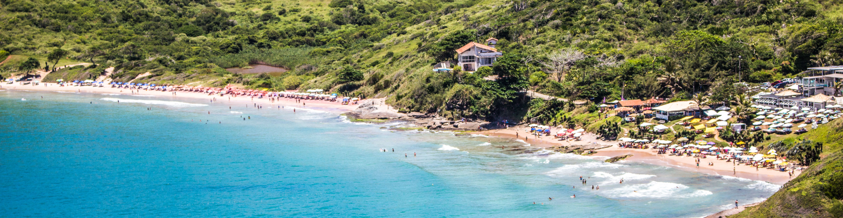 Vista panorâmica da costa de Búzios, no Rio de Janeiro, em um dia ensolarado. As ondas se quebram na praia, que é cercada pela vegetação local.