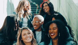 Imagem com seis mulheres sentadas em uma escada. A mulheres estão conversando e rindo em conjunto.