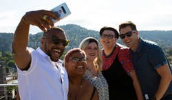 Imagem de um grupo de amigos, sendo dois homens e três mulheres, sorrindo para uma selfie.
