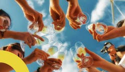 Imagem de um grupo de pessoas brindando em direção a um céu azul.
