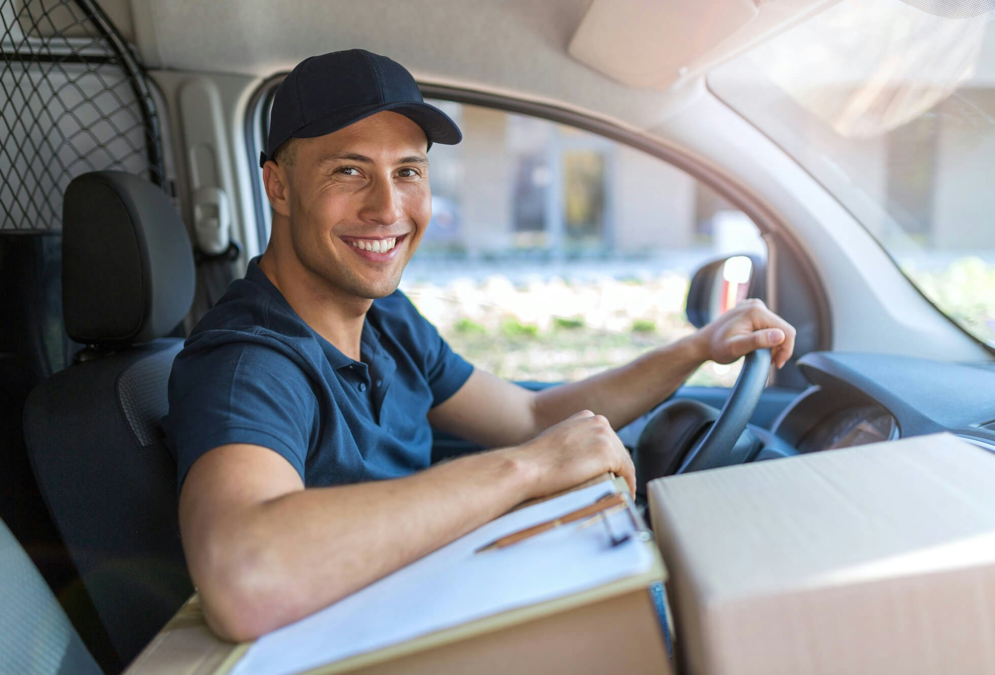 Portrait of a male driver in the driver's seat of a van. He is looking at the camera and sitting next to some packages.