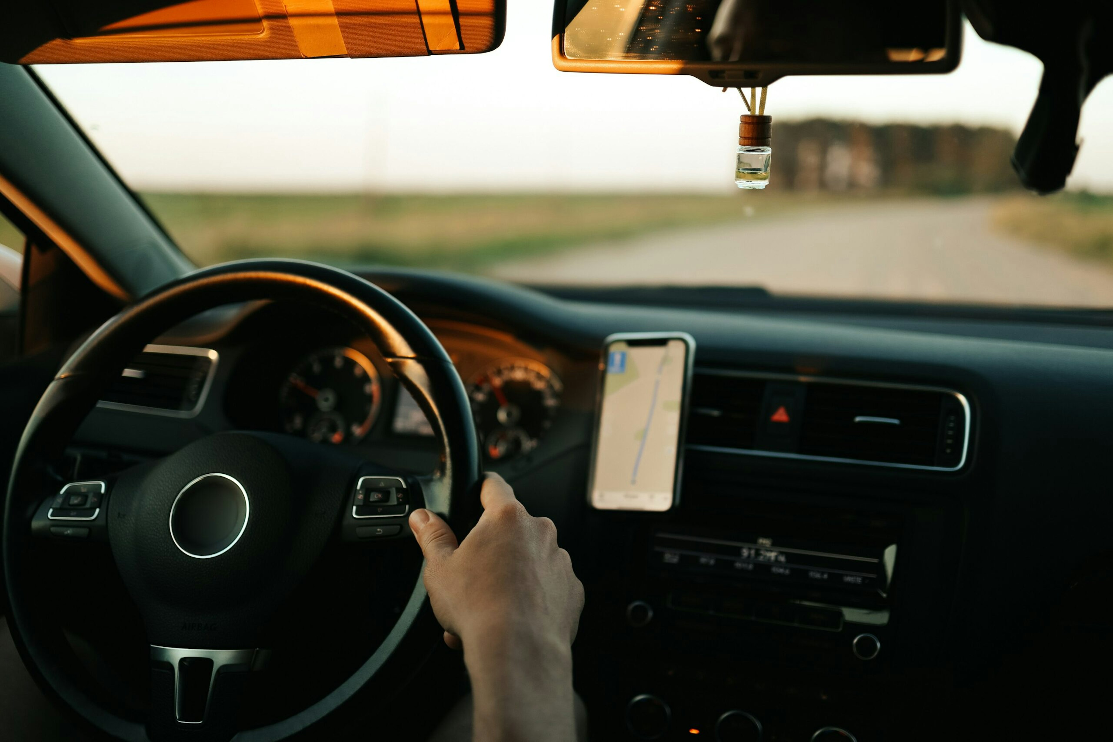 Close-up f hands on a steering wheel with a mobile phone showing route navigation