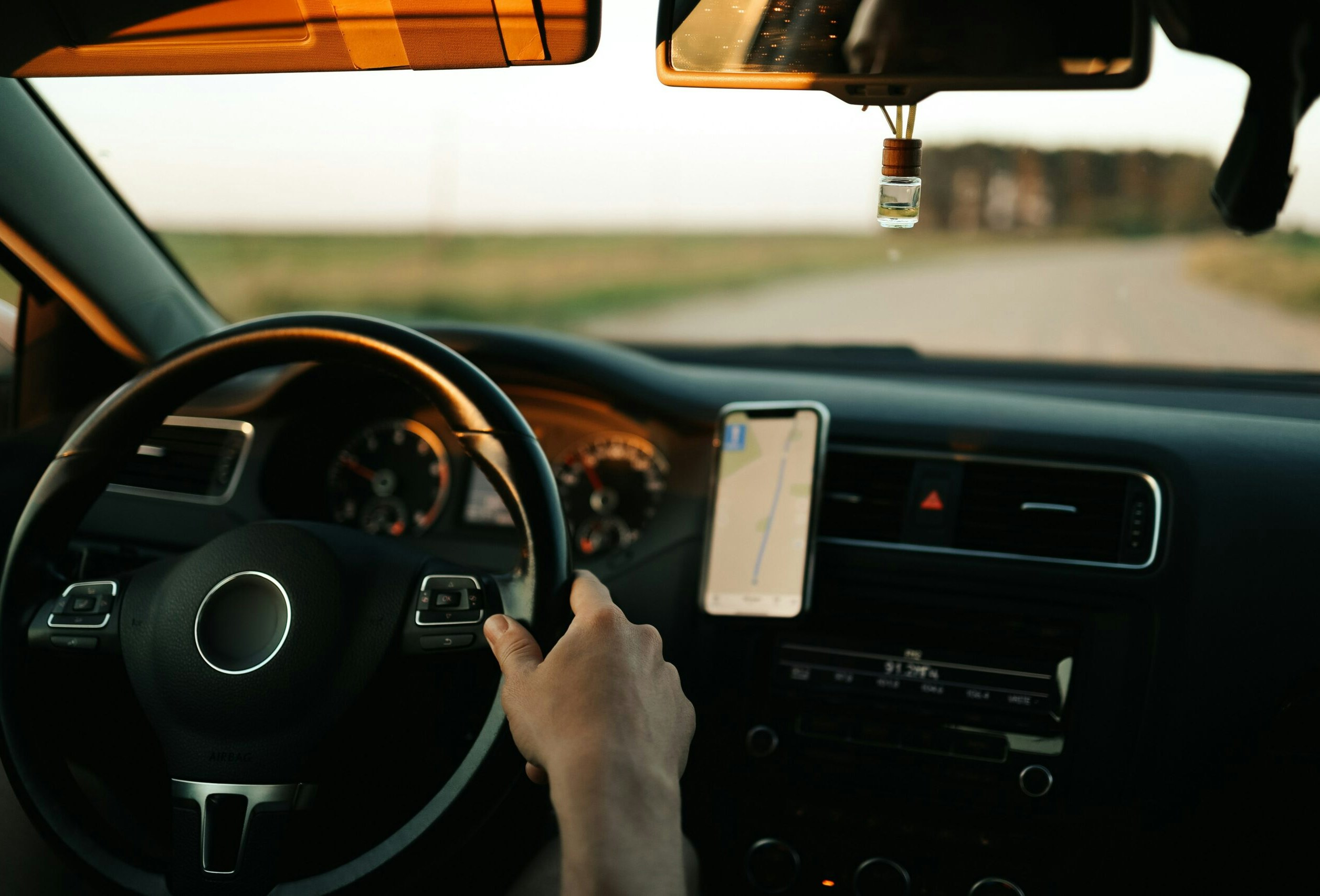 Close-up f hands on a steering wheel with a mobile phone showing route navigation