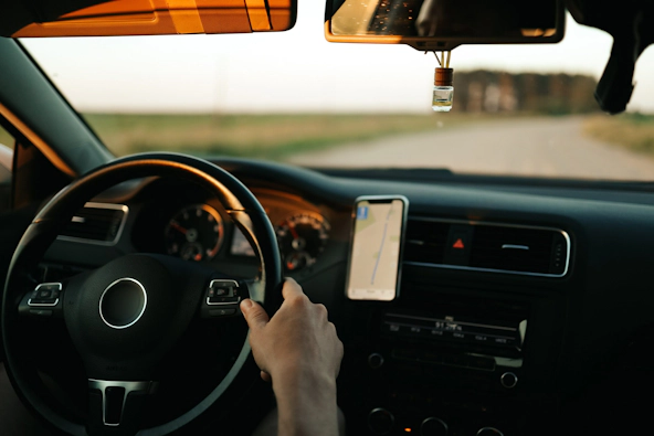 Close-up f hands on a steering wheel with a mobile phone showing route navigation