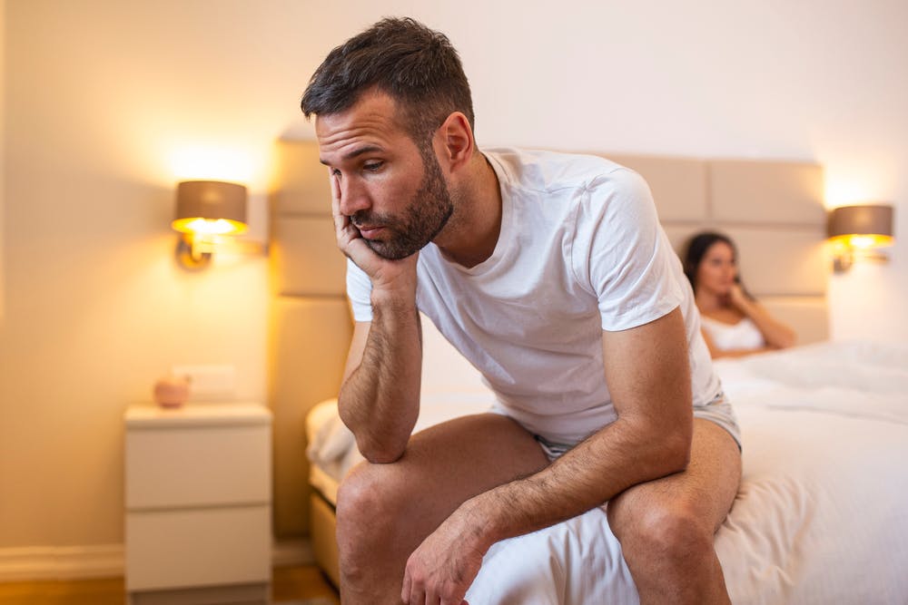 couple looking upset and stressed while sitting next to each other in bed