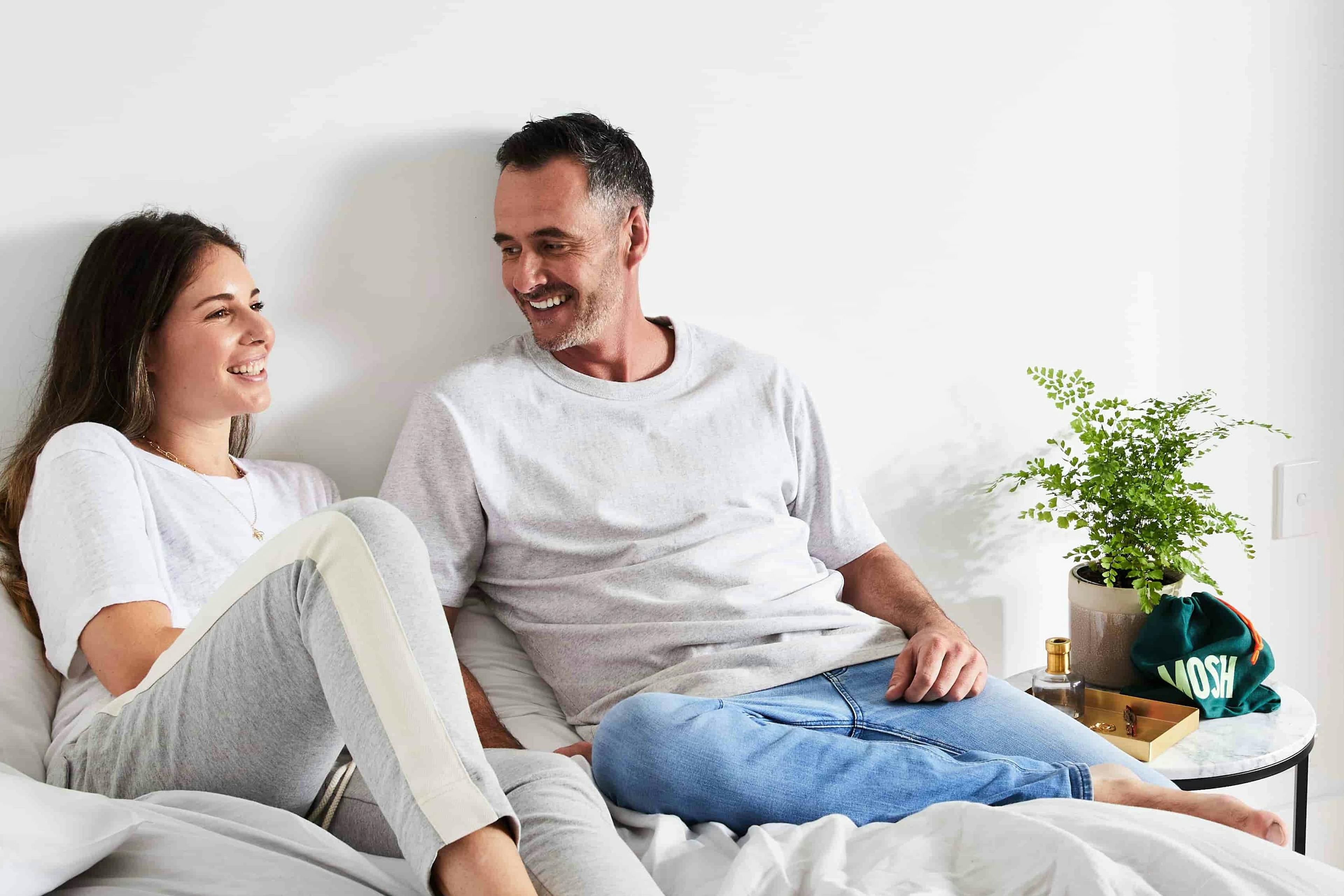 Couple smiling in bed with Mosh bag on side table