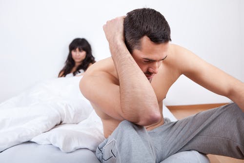 Man looking distressed in bed with his partner looking upset