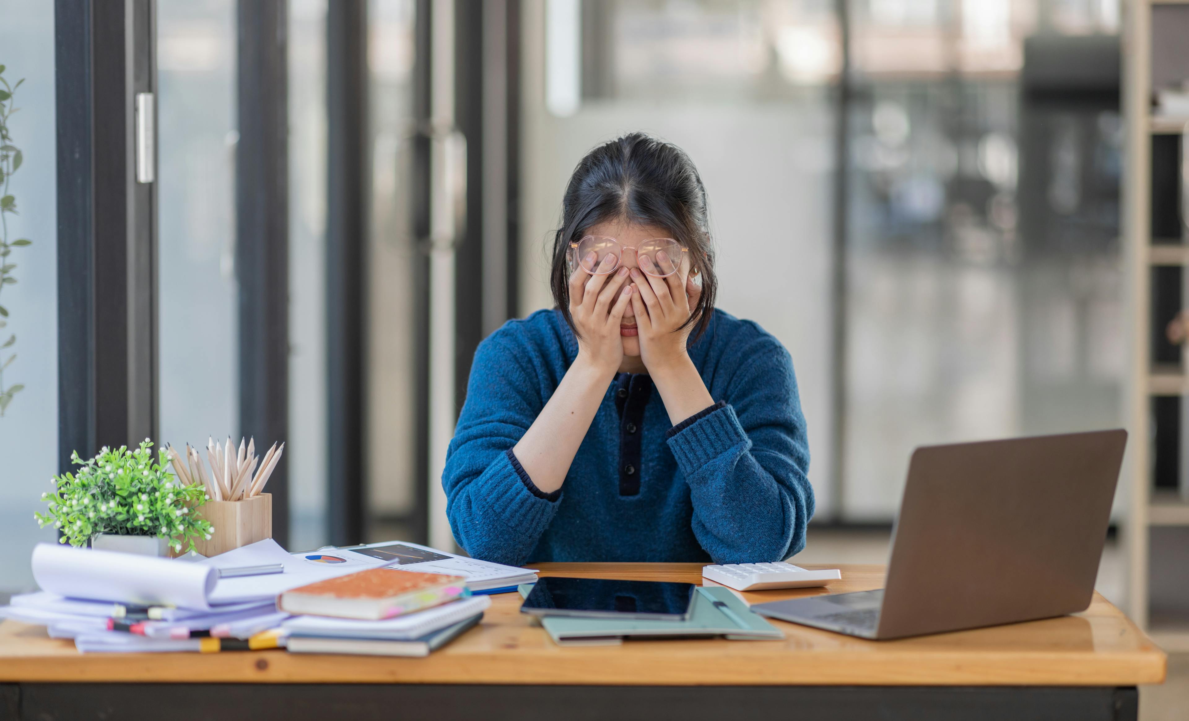 Woman head in hands, stressed and exhausted at her work desk
