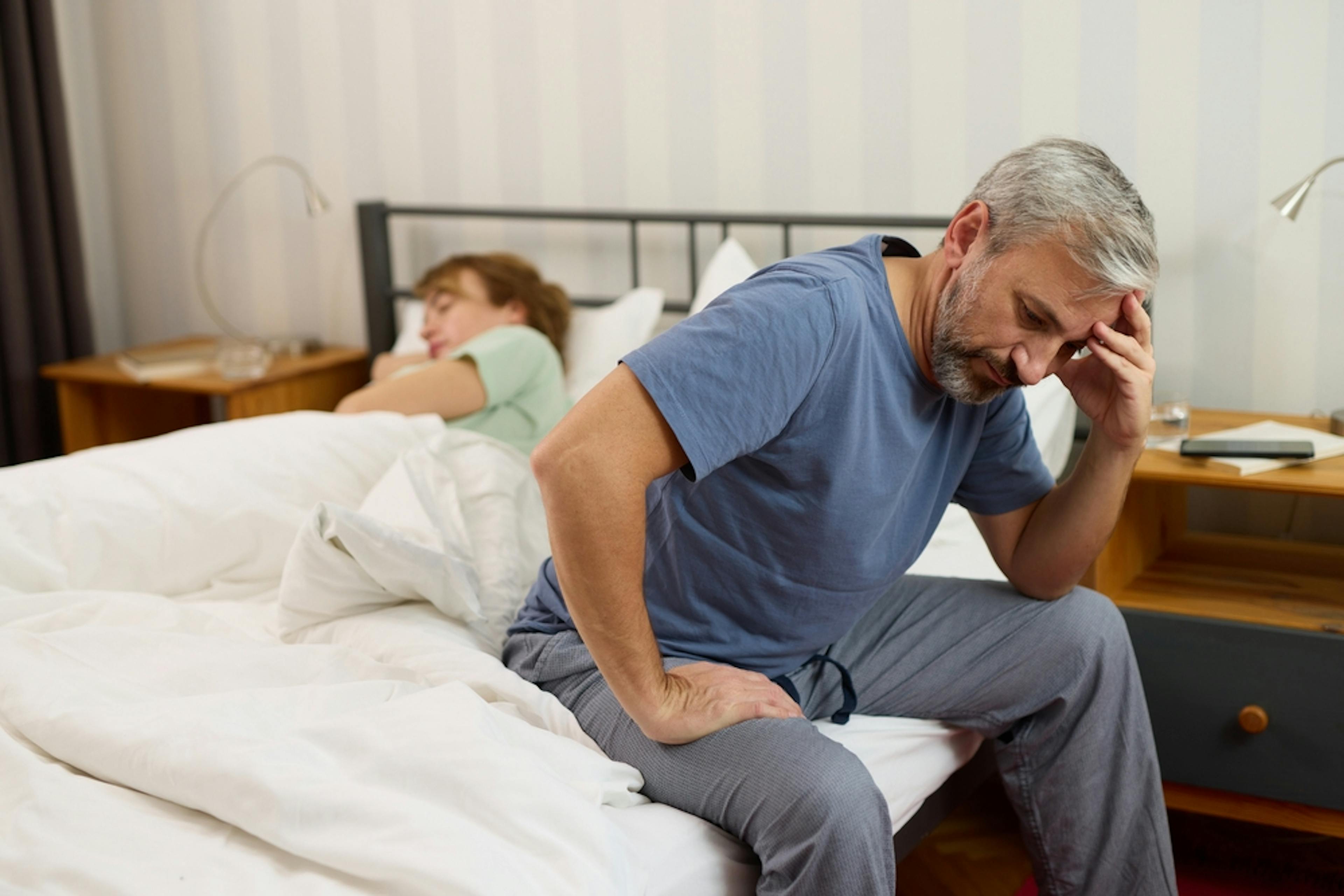 man that looks upset seating on his bed next to his partner