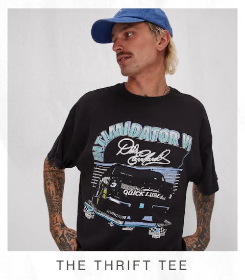 Image of male model in studio, he is looking to his right. He is wearing the Thrift Tee; Burnout Black and Classic Cap; Baddie Blue. Test reads ''The Thrift Tee'.
